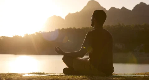 man-meditating-doing-yoga-by-lake-and-mountains-at-2023-03-17-18-02-48-utc-scaled